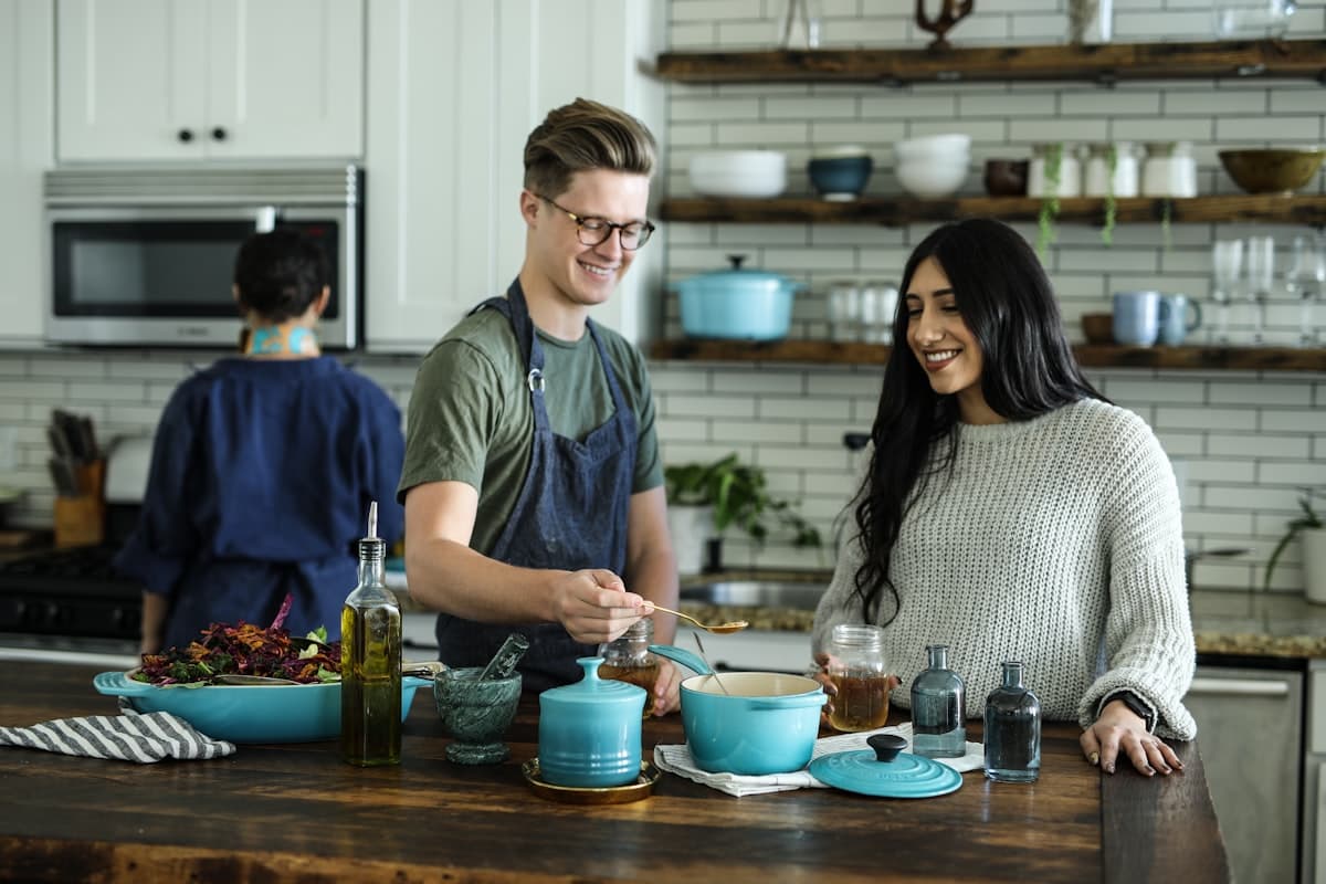 Three young adults cooking and tasting food together at a kitchen island in a modern home