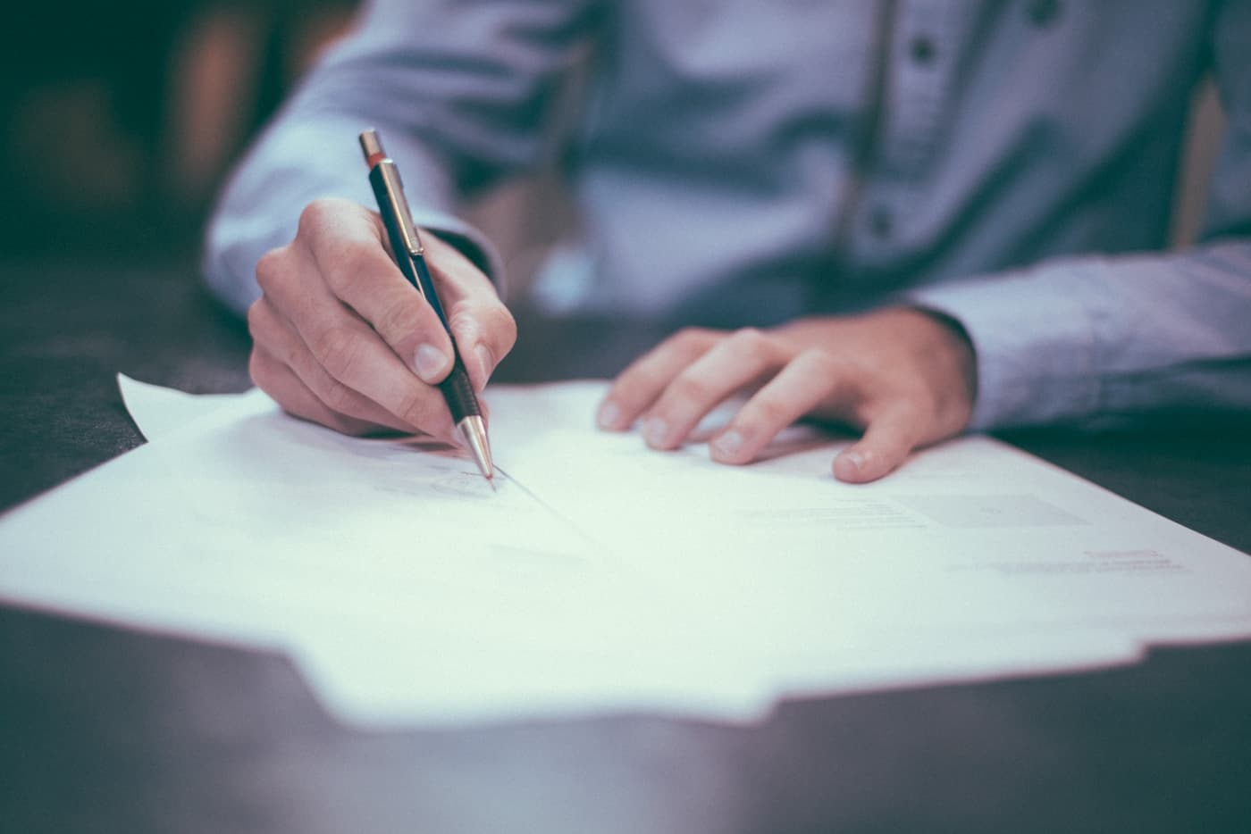 Close-up of hands signing a document with a pencil on a desk, business shirt sleeves visible
