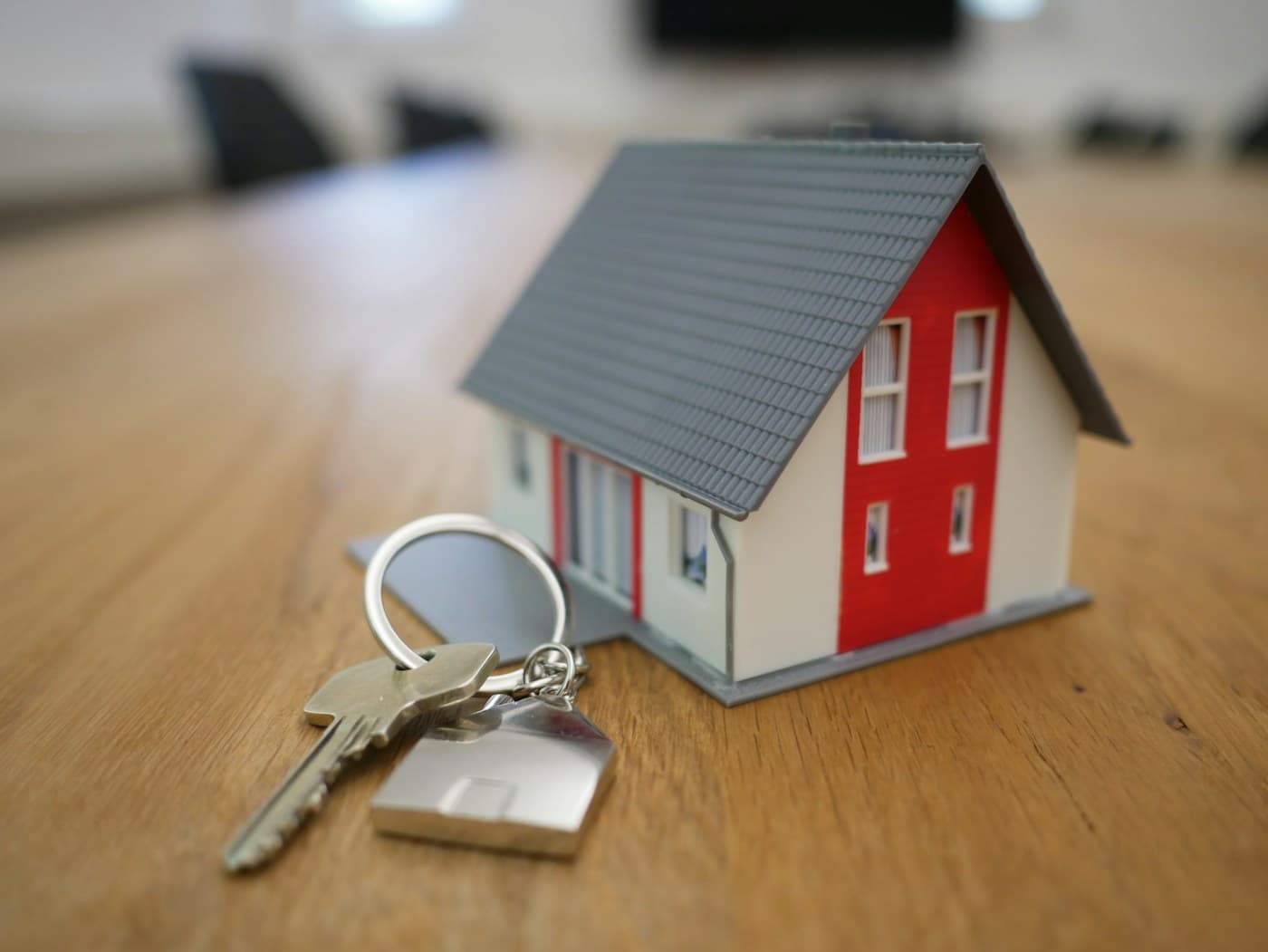 Miniature model house with silver keys on a light wooden table, shallow depth of field