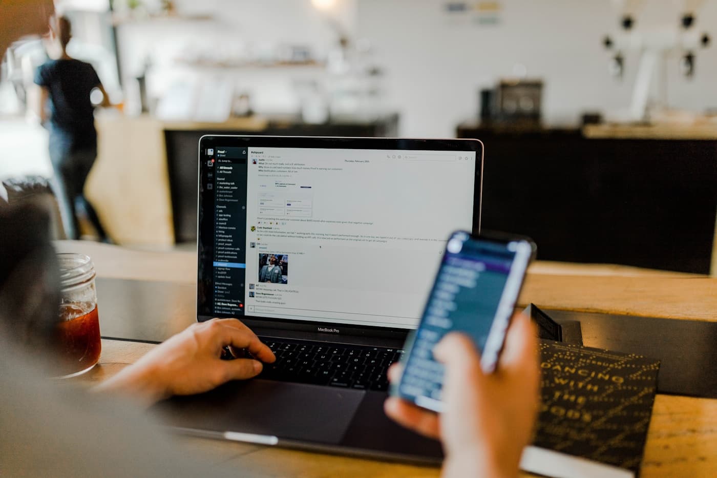 Laptop open on a desk beside a notebook, pen, and smartphone on a wooden table