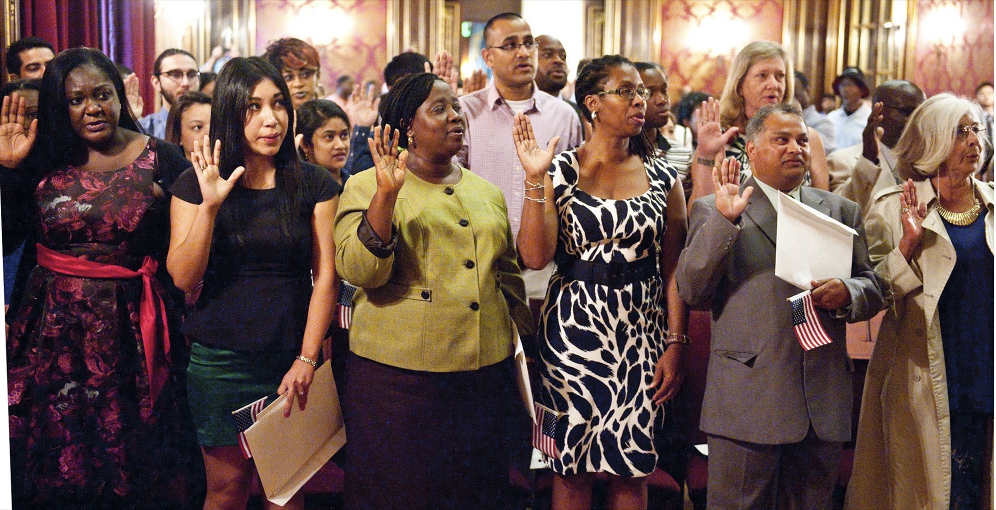 New U.S. citizens raise their right hands during the oath at a July 4 naturalization ceremony