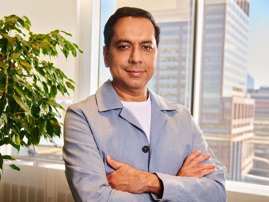 Chirantan CJ Desai in a light jacket, arms crossed, in an office with a city window behind him