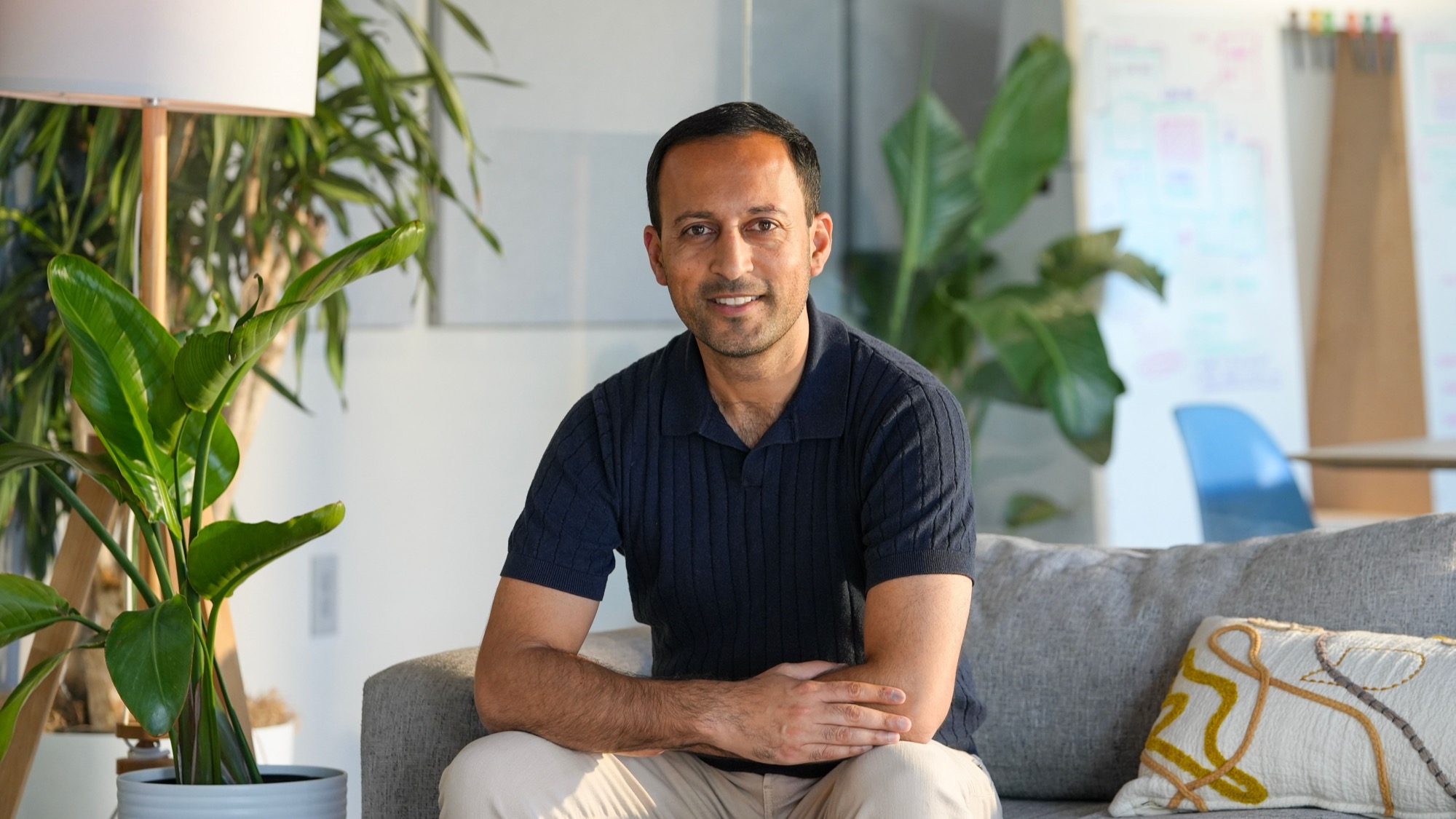 Gagan Biyani seated on a sofa in a bright office, wearing a navy polo