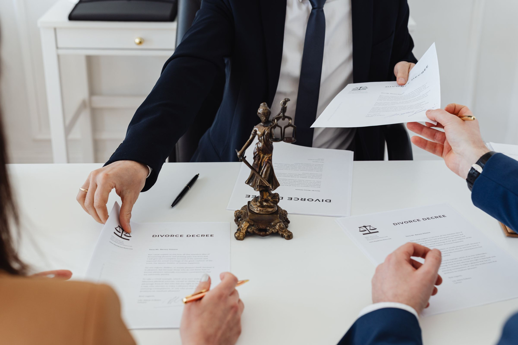 Hands exchanging divorce decree documents across a desk with a justice statue and pens