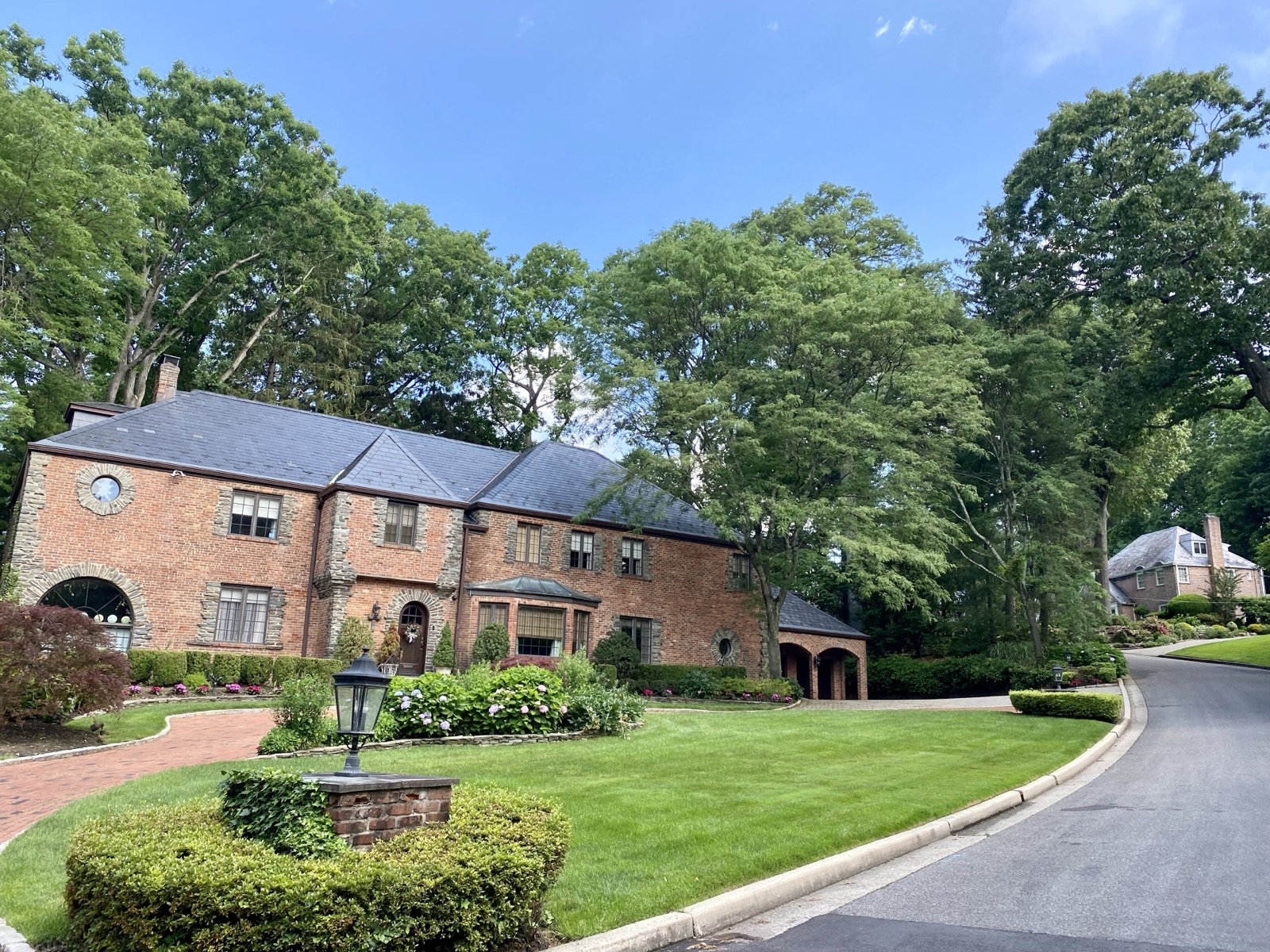 Brick suburban house with a green front lawn on a residential street in Manhasset, New York
