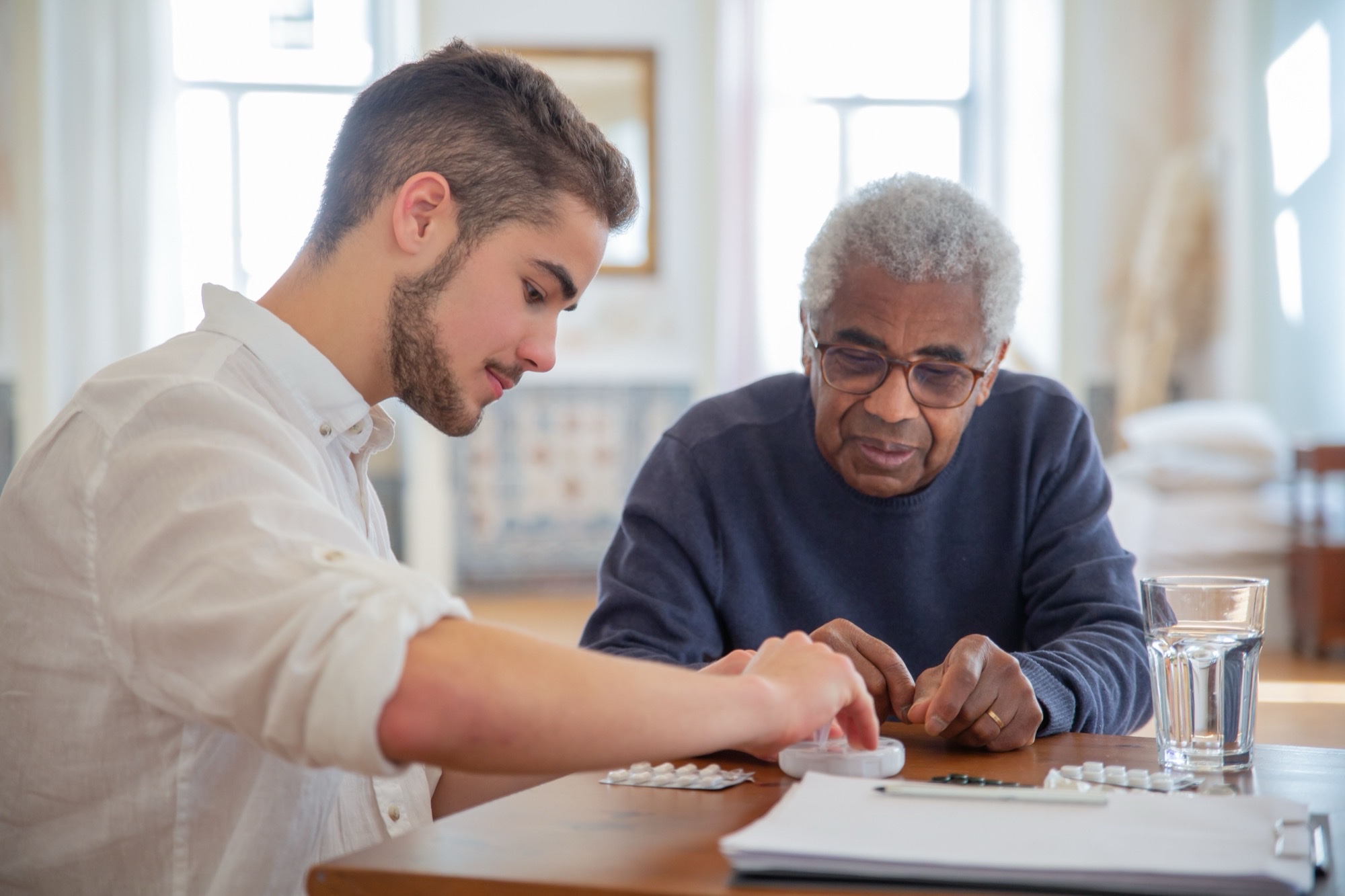 Adult child helping an older parent sort medication and paperwork at a kitchen table