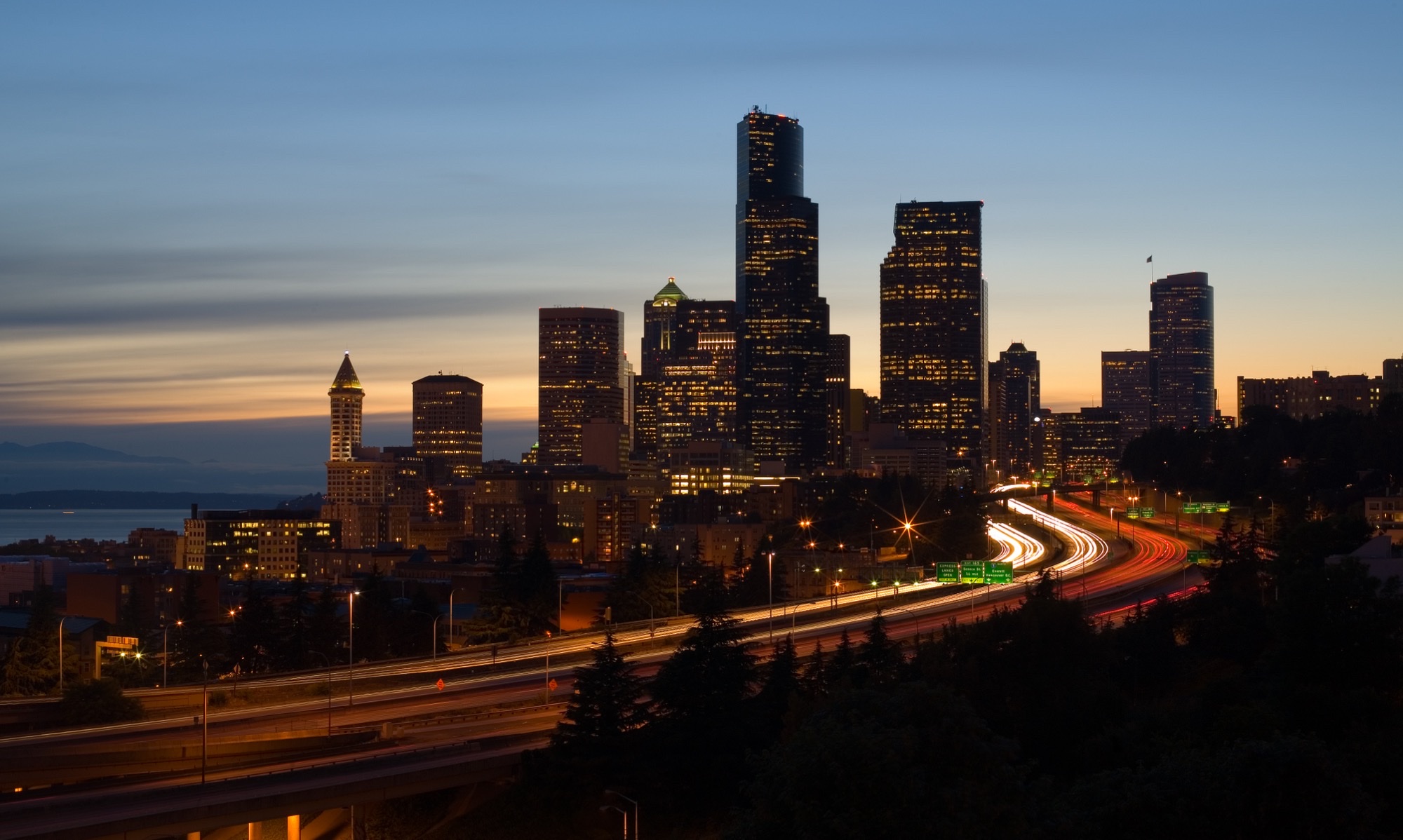 Seattle downtown skyline at dusk over Interstate 5, with lighted towers and Puget Sound beyond
